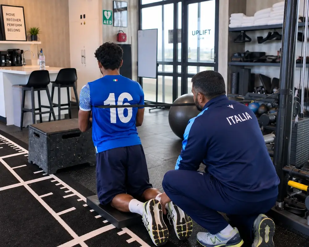 Thihan Chandramohan guiding a player through a banded kneeling exercise in the Uplift Gym rehabilitation space